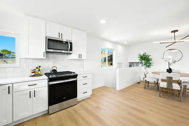 a kitchen with stainless steel appliances a white stove top oven a sink dishwasher and white cabinets with wooden floor