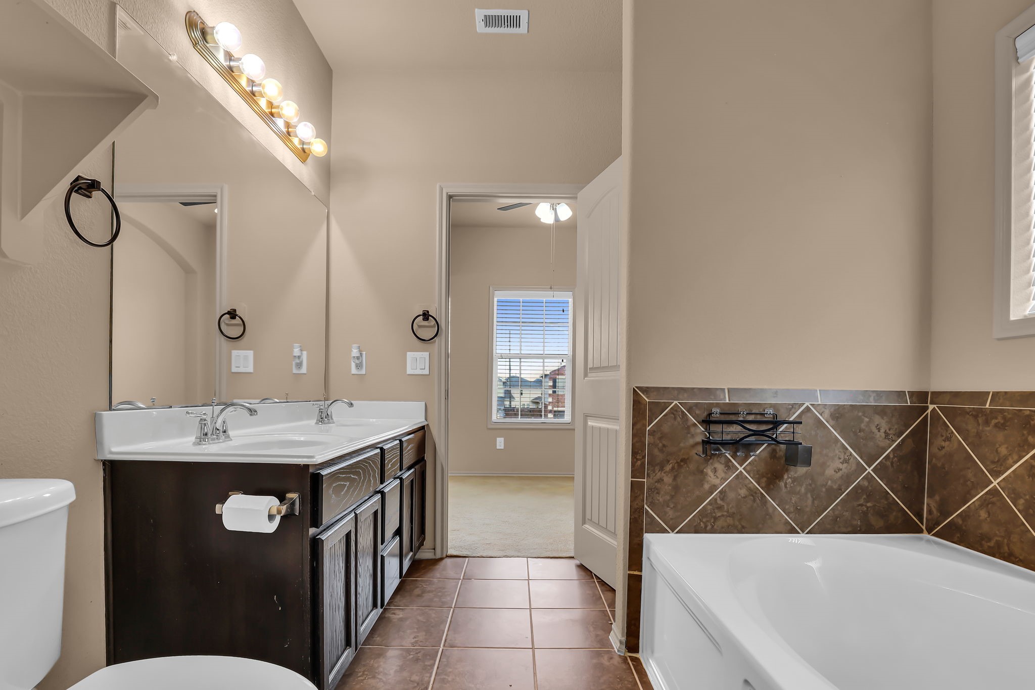 21307 Carleen Creek Trail Spring, TX 77379 - Photo 21 of 25 Primary Bathroom has a dual-sink vanity with ample storage, a large mirror with stylish lighting, a tiled soaking tub, and access to a well-lit bedroom.
