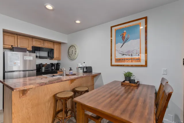 a kitchen with stainless steel appliances granite countertop a refrigerator a stove a sink a dining table and chairs with wooden floor