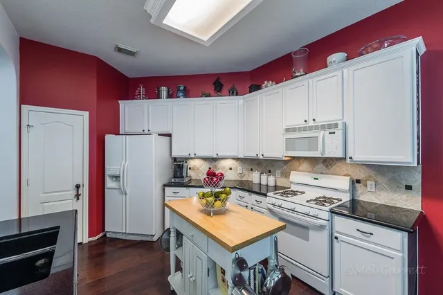 a kitchen with granite countertop a refrigerator a sink dishwasher and white cabinets with wooden floor