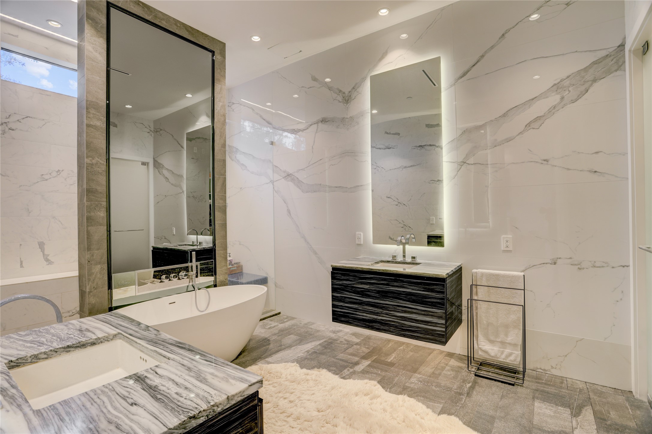 1807 Indiana Street Houston, TX 77006 - Photo 24 of 35 Primary En-Suite Bath: Spa-like primary retreat clad in book-matched tile walls, featuring separate his-and-her vanities with premium marble countertops, a freestanding soaking tub, and vertical backlit LED mirrors.