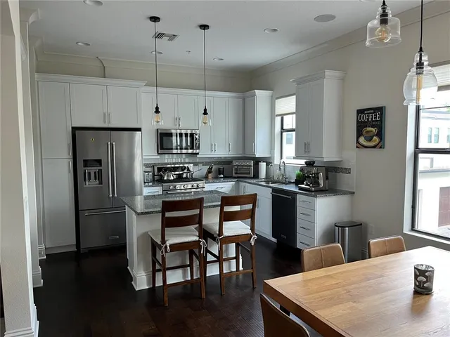 a kitchen with granite countertop a refrigerator a stove a sink a dining table and chairs