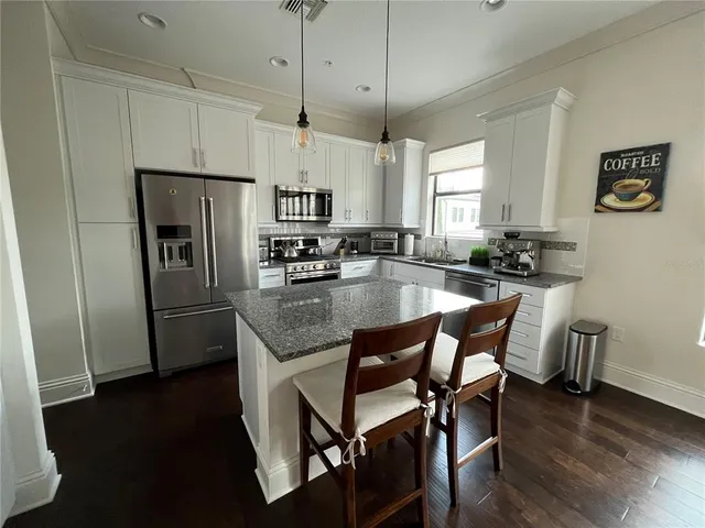 a kitchen with stainless steel appliances granite countertop a refrigerator a sink a stove a dining table and chairs
