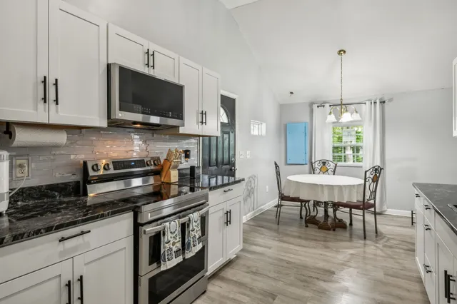 a kitchen with stainless steel appliances granite countertop a stove top oven a sink dishwasher a dining table and chairs with wooden floor