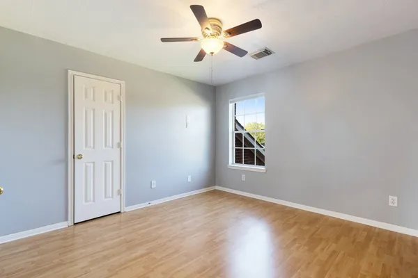 an empty room with wooden floor chandelier fan and windows