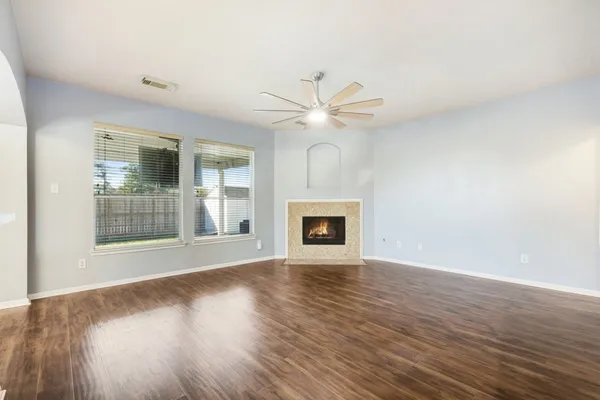 an empty room with wooden floor a ceiling fan and windows