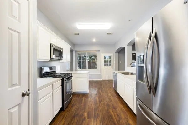 a kitchen with stainless steel appliances a refrigerator a stove a sink dishwasher a oven with white cabinets and wooden floor