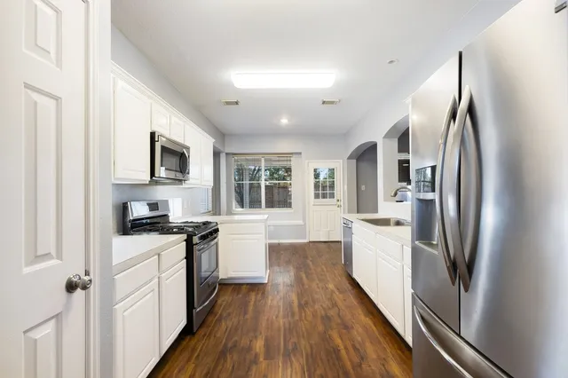 a kitchen with stainless steel appliances a refrigerator a stove a sink dishwasher a oven with white cabinets and wooden floor