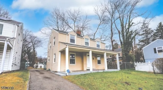 a view of a white house with a large windows and a yard with plants and large tree