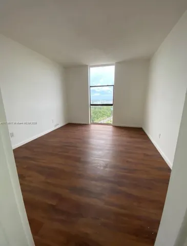 a view of an empty room with a window and wooden floor