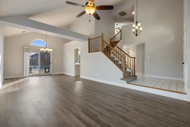 a view of a livingroom with wooden floor stairs and a chandelier fan