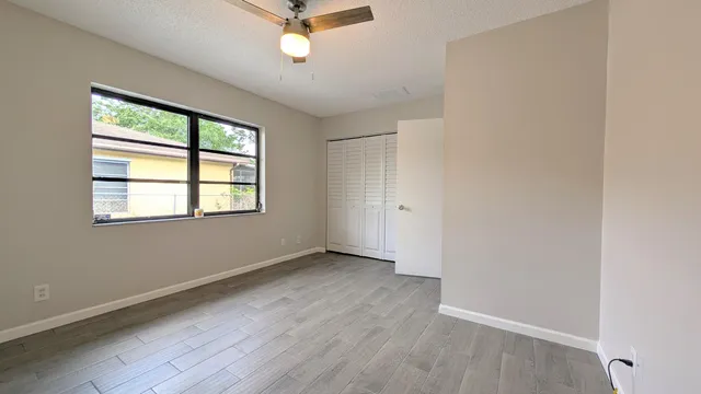an empty room with wooden floor fan and windows