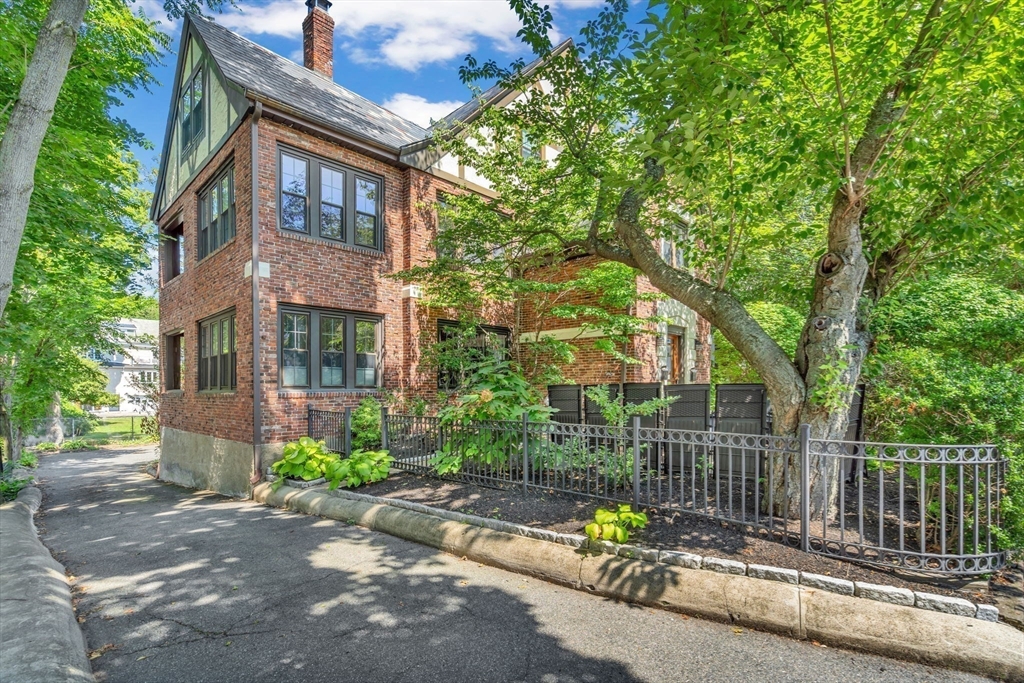 27 Newell Road, Unit 2 Brookline, MA 02446 - Photo 36 of 41 a view of a brick house with a small yard and large trees