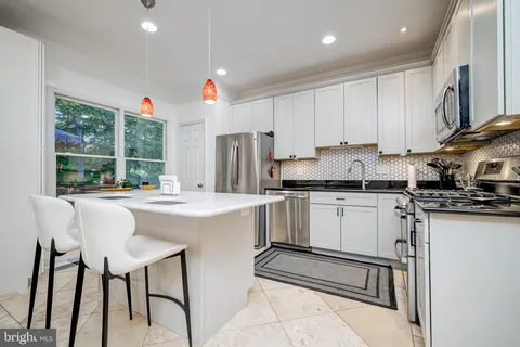a kitchen that has a lot of white cabinets and stainless steel appliances