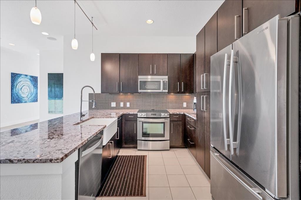 1101 Ivean Pearson Road, Unit A102 Lago Vista, TX 78645 - Photo 4 of 31 Kitchen with stainless steel appliances, light stone countertops, a peninsula, light tile patterned floors, and dark brown cabinets