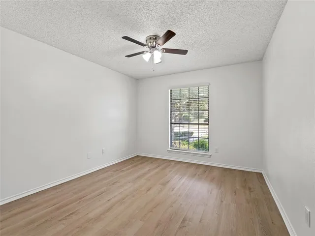 an empty room with wooden floor fan and windows