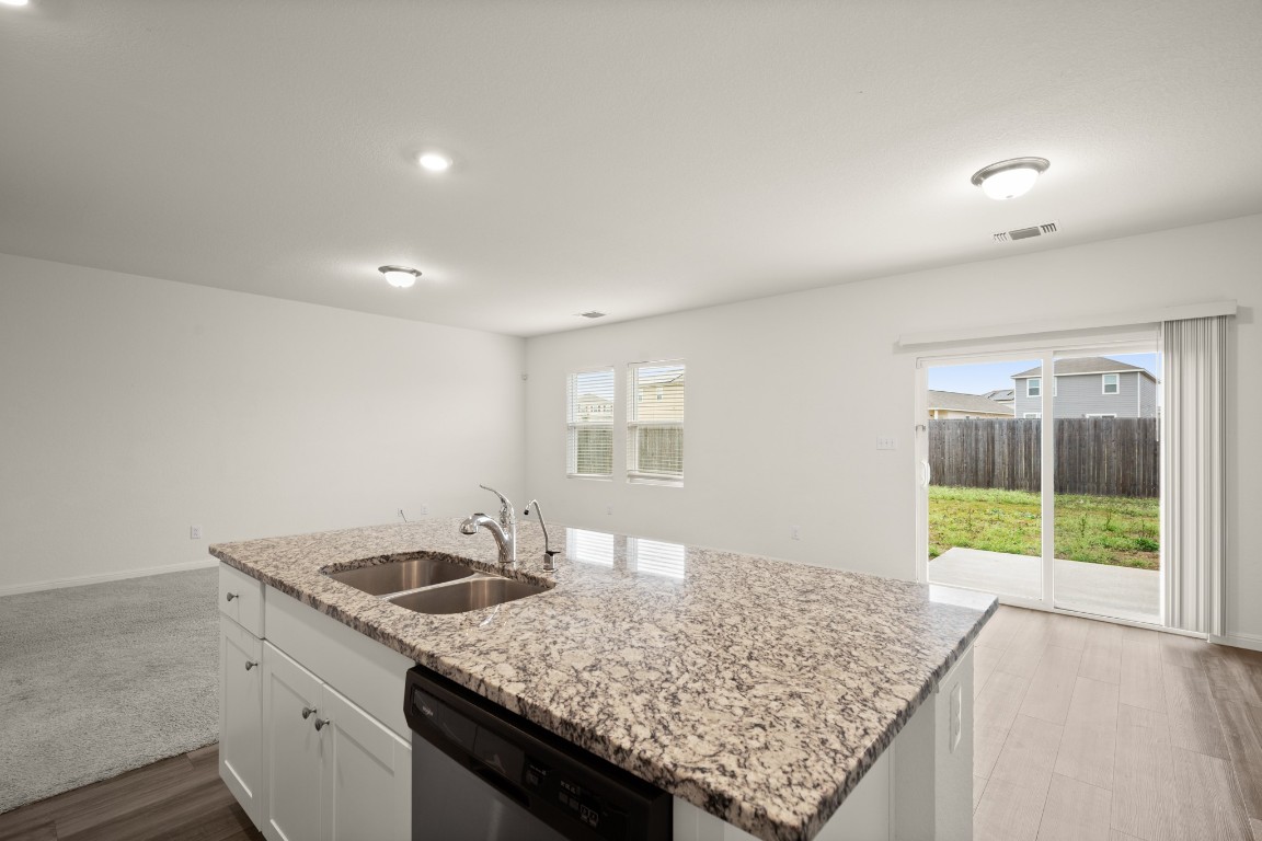 109 Gray Fox Loop Hutto, TX 78634 - Photo 25 of 28 Kitchen featuring white cabinets, light stone counters, stainless steel dishwasher, a center island with sink, and open floor plan