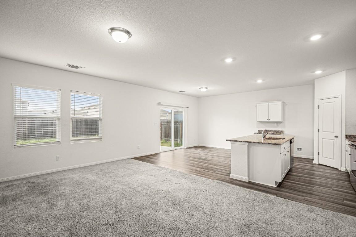 109 Gray Fox Loop Hutto, TX 78634 - Photo 26 of 28 Kitchen with open floor plan, a center island with sink, a textured ceiling, dark stone countertops, and dark carpet