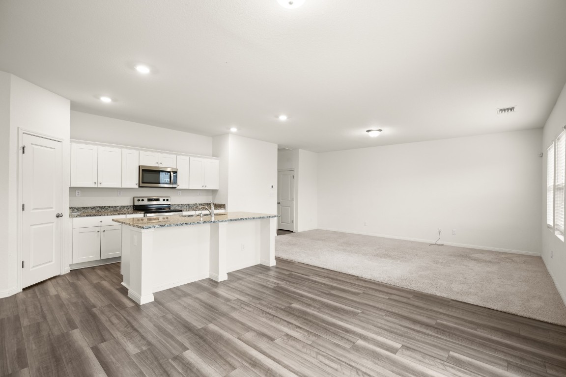 109 Gray Fox Loop Hutto, TX 78634 - Photo 28 of 28 Kitchen with white cabinets, an island with sink, open floor plan, light stone counters, and appliances with stainless steel finishes