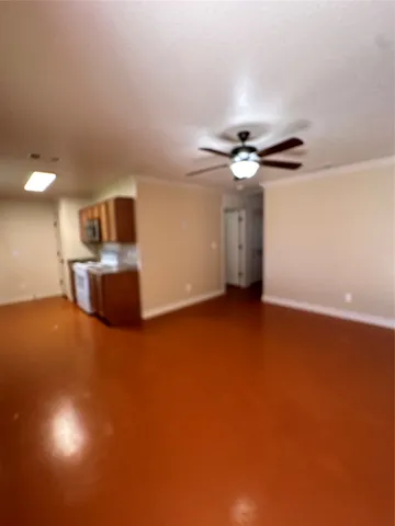 a view of an empty room with a ceiling fan and kitchen view