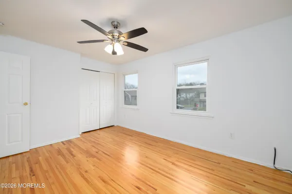 a view of an empty room with wooden floor and a ceiling fan