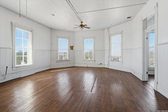 an empty room with wooden floor and windows with curtains