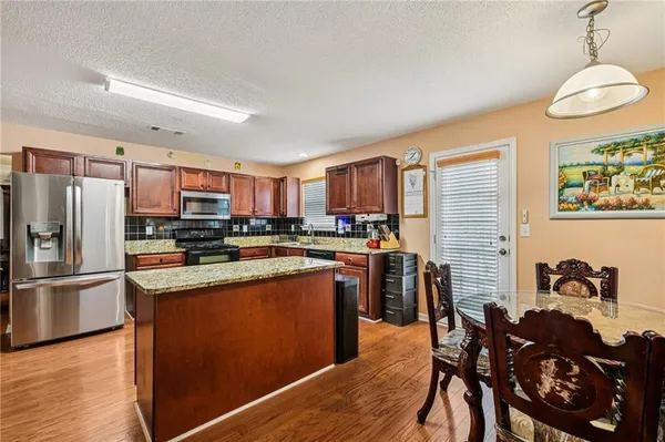 a kitchen with stainless steel appliances granite countertop a refrigerator a stove a sink dishwasher and a dining table with wooden floor