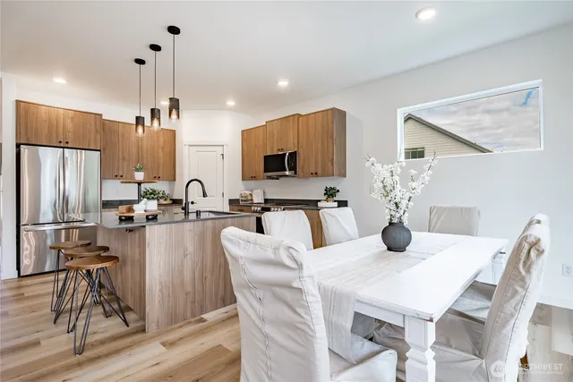 a kitchen with stainless steel appliances kitchen island granite countertop a dining table chairs and a refrigerator