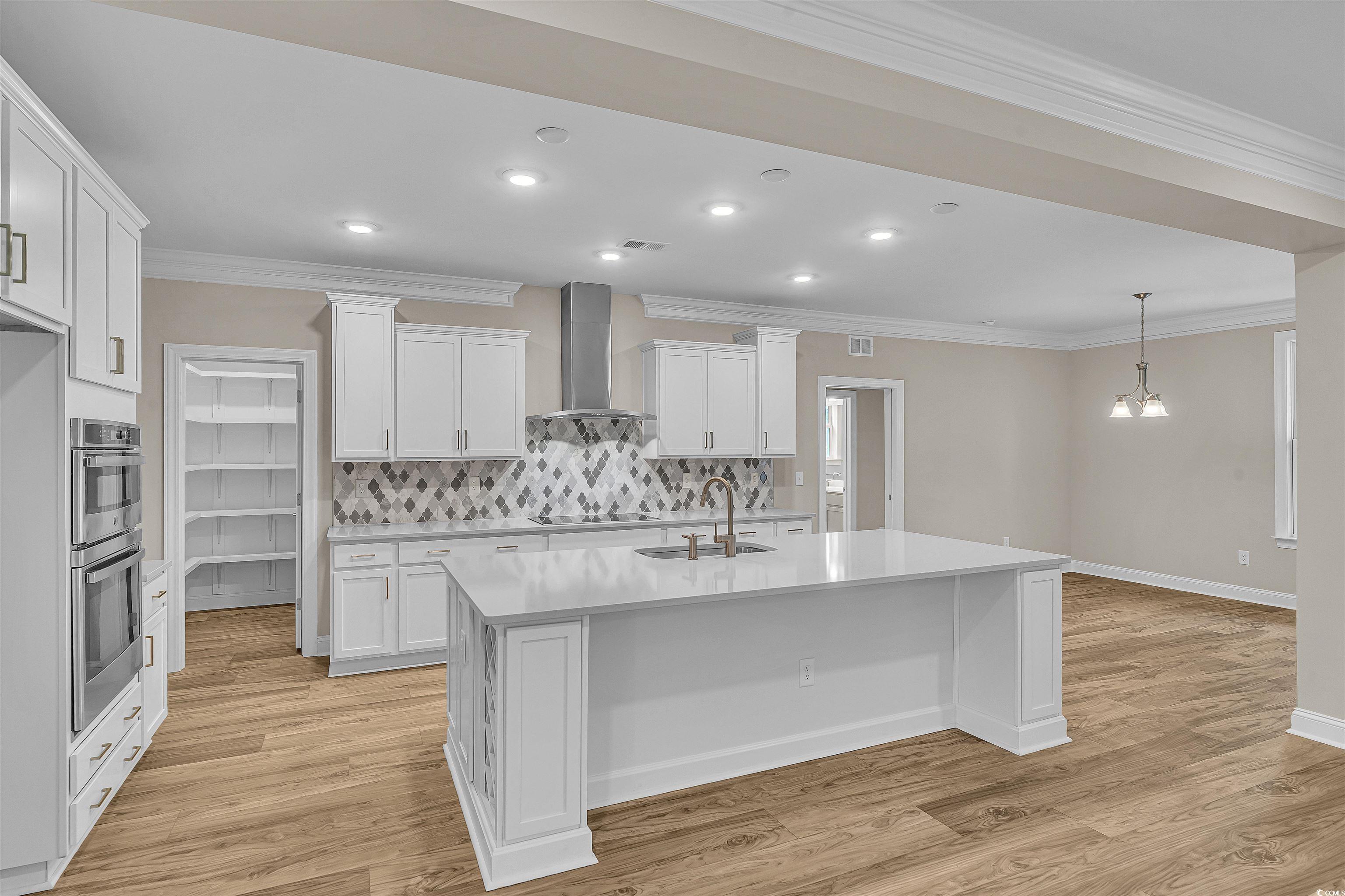 550 Beachside Circle Calabash, NC 28467 - Photo 17 of 39 Kitchen with light hardwood / wood-style floors, white cabinetry, wall chimney exhaust hood, and an island with sink