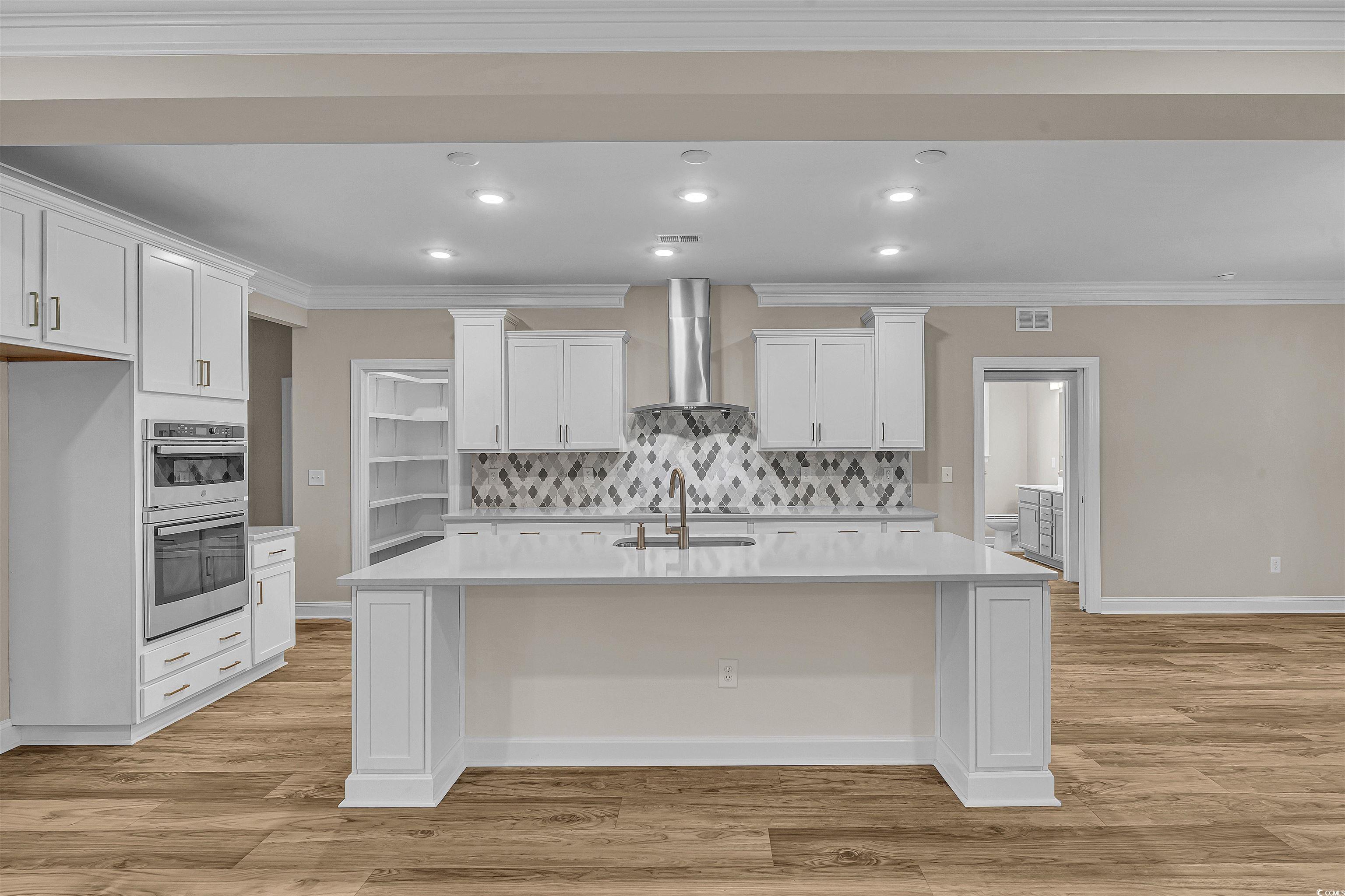 550 Beachside Circle Calabash, NC 28467 - Photo 18 of 39 Kitchen with decorative backsplash, wall chimney exhaust hood, an island with sink, and white cabinetry