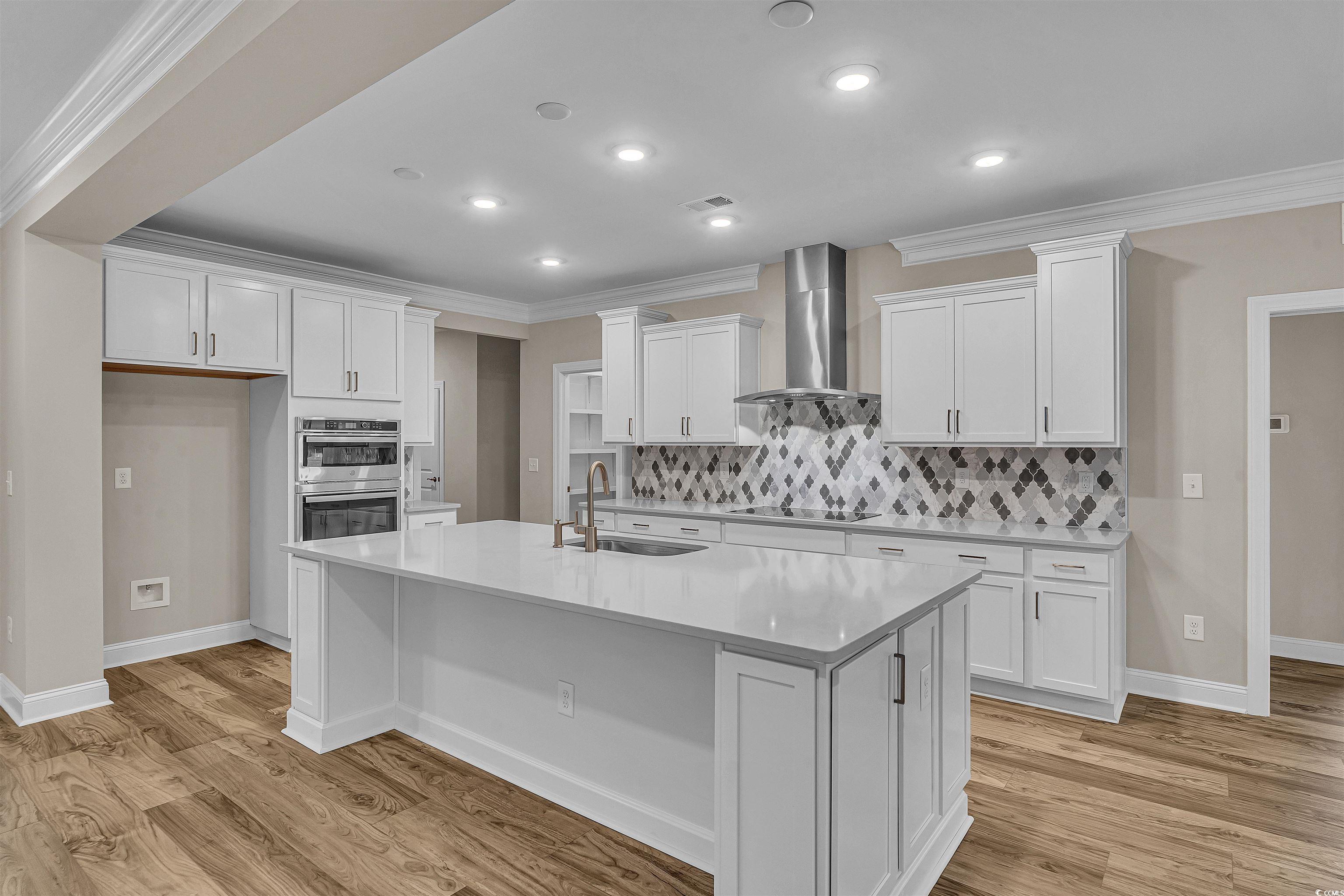 550 Beachside Circle Calabash, NC 28467 - Photo 19 of 39 Kitchen with white cabinetry, sink, black cooktop, a kitchen island with sink, and wall chimney range hood