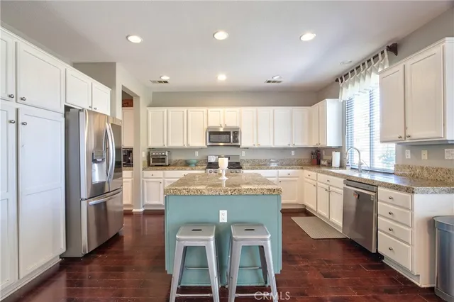 a kitchen with stainless steel appliances granite countertop a refrigerator a sink dishwasher a stove and white cabinets with wooden floor