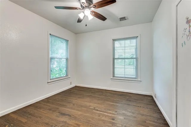 an empty room with wooden floor chandelier fan and windows