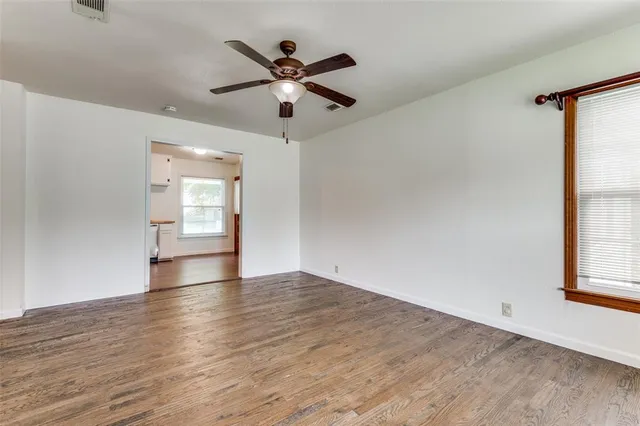 an empty room with wooden floor fan and windows