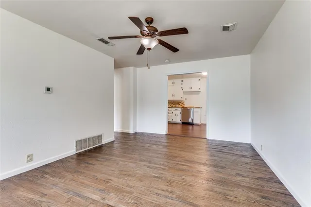 a view of an empty room with wooden floor and a ceiling fan