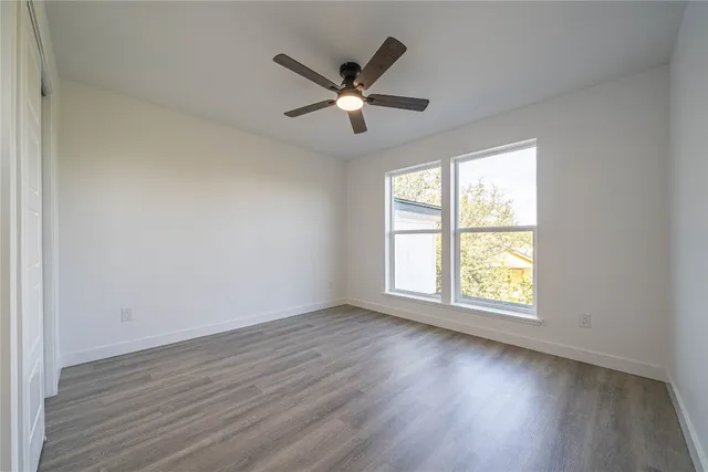 an empty room with wooden floor fan and windows