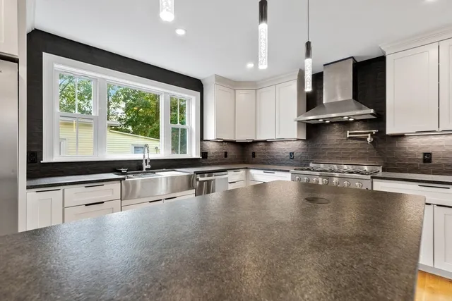 a large kitchen with stainless steel appliances a large counter top a stove a sink and a large window