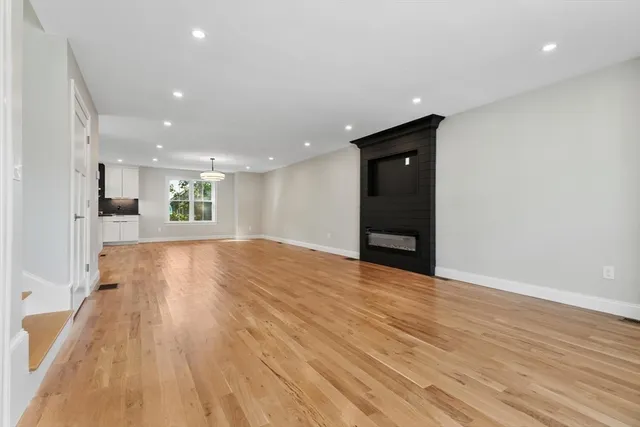 a view of an empty room with wooden floor and a kitchen