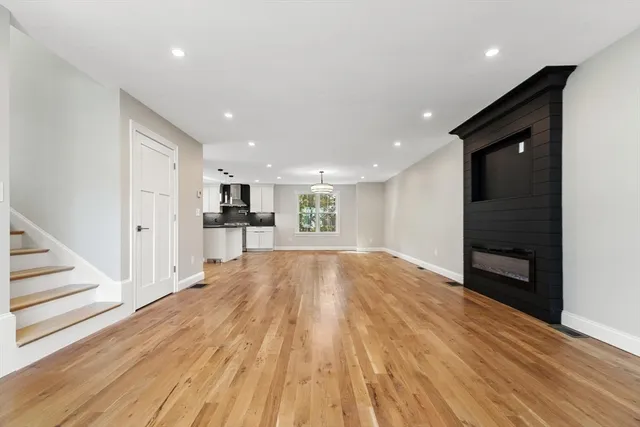 a view of empty room with wooden floor and kitchen