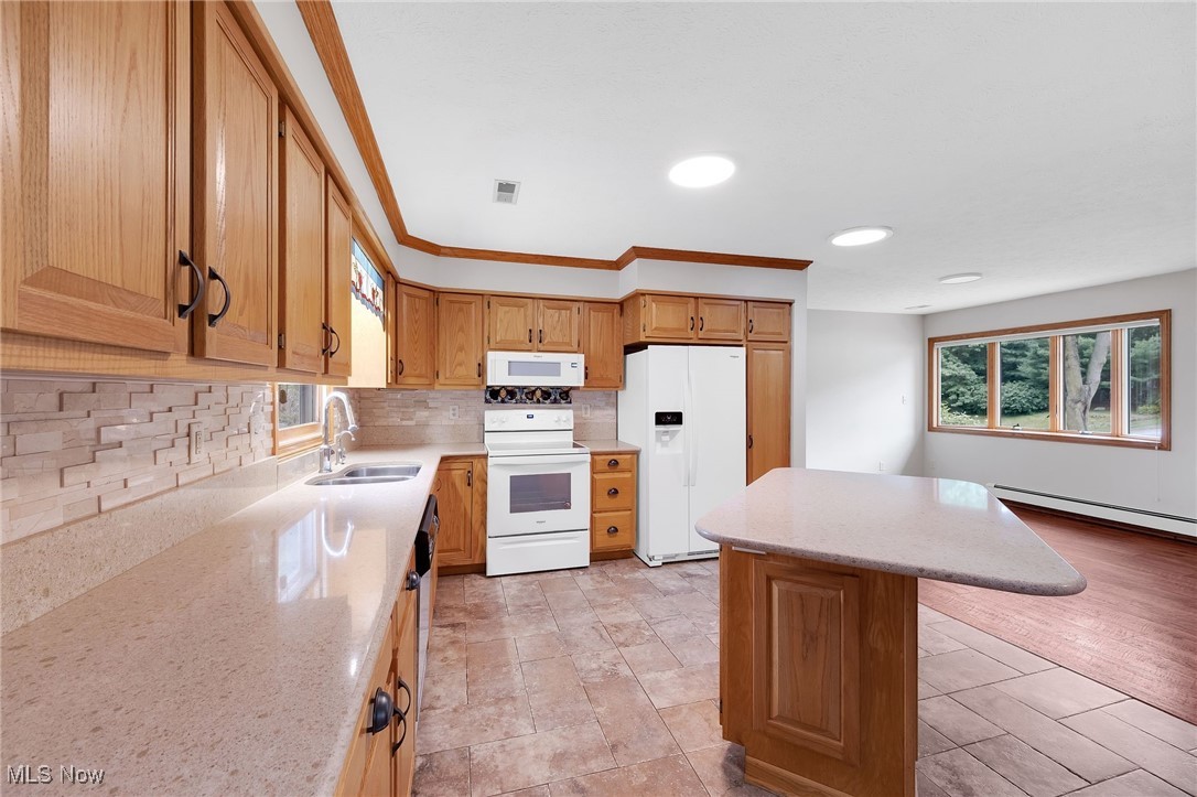 7923 Zigler Road Sterling, OH 44276 - Photo 6 of 31 Kitchen with white appliances, a baseboard heating unit, decorative backsplash, a kitchen island, and light stone counters