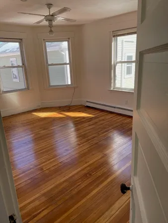 an empty room with wooden floor fan and windows