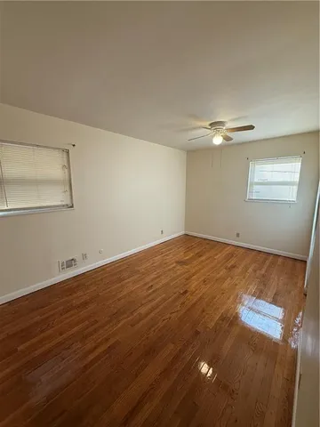 an empty room with wooden floor fan and windows