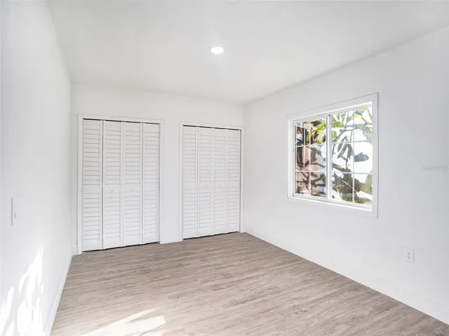 an empty room with wooden floor closet and windows