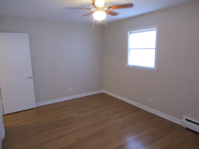 an empty room with wooden floor fan and window