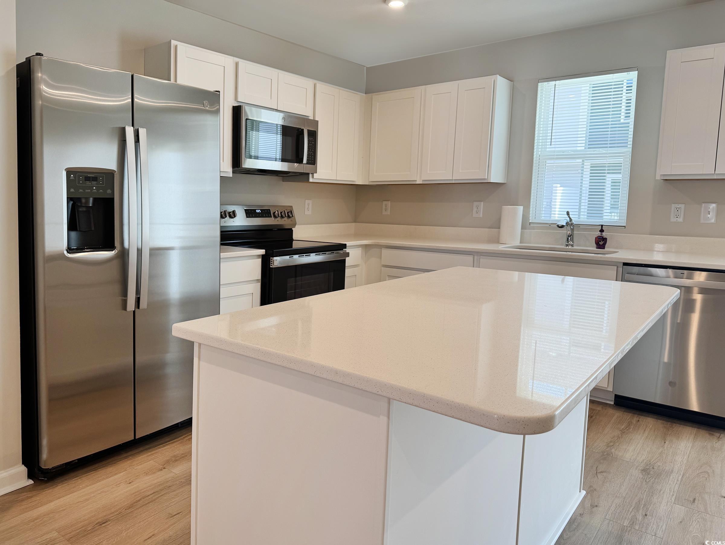 157 B Villa Grande Street, Unit B Myrtle Beach, SC 29579 - Photo 2 of 28 Kitchen featuring appliances with stainless steel finishes, a center island, white cabinets, light wood-type flooring, and light stone counters