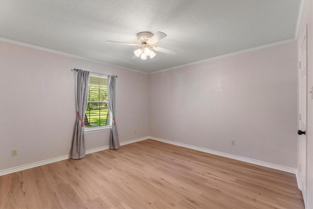 116 Meadowood Road Enchanted Oaks, TX 75156 - Photo 27 of 37 Spacious room featuring wood-finish flooring, a ceiling fan with integrated lighting, a window with exterior views, crown molding, and white baseboards
