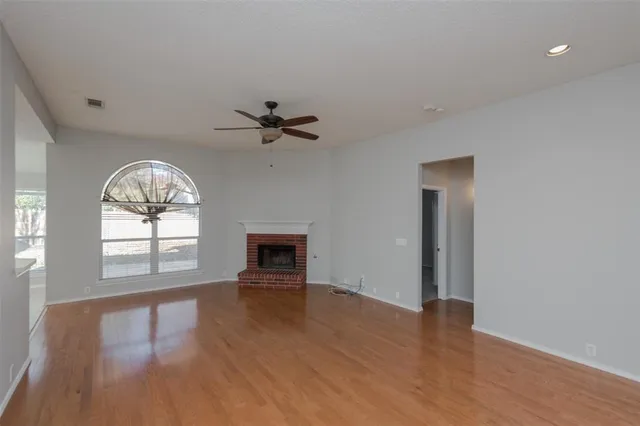 an empty room with wooden floor fan and windows