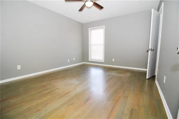 an empty room with wooden floor chandelier fan and windows