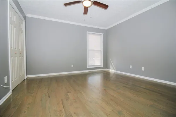 an empty room with wooden floor chandelier fan and windows