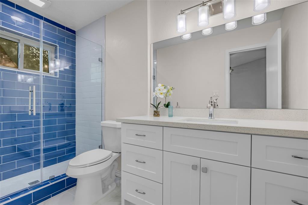 25703 Old Carriage Lane Spring, TX 77373 - Photo 18 of 25 Master Bathroom featuring a glass-enclosed shower with blue subway tiles, a white vanity with granite countertop, and plenty of overhead lighting